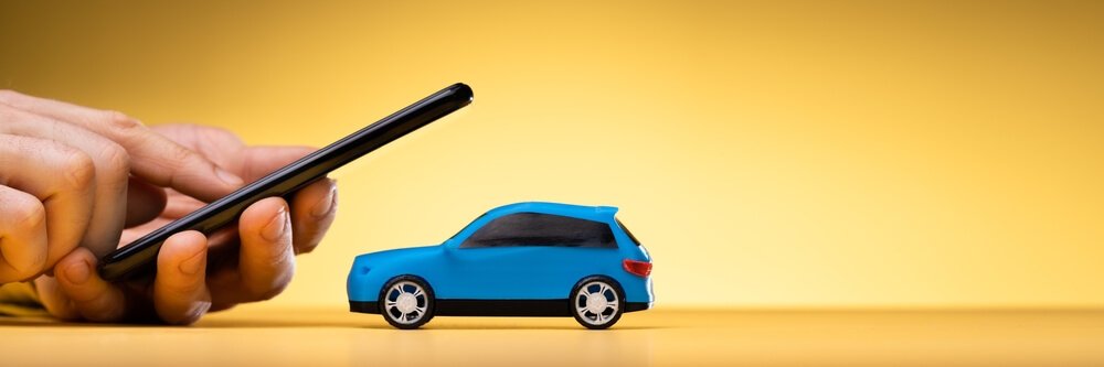 Bilde av en blå bil og en stor hånd som holder en smarttelefon over bilen