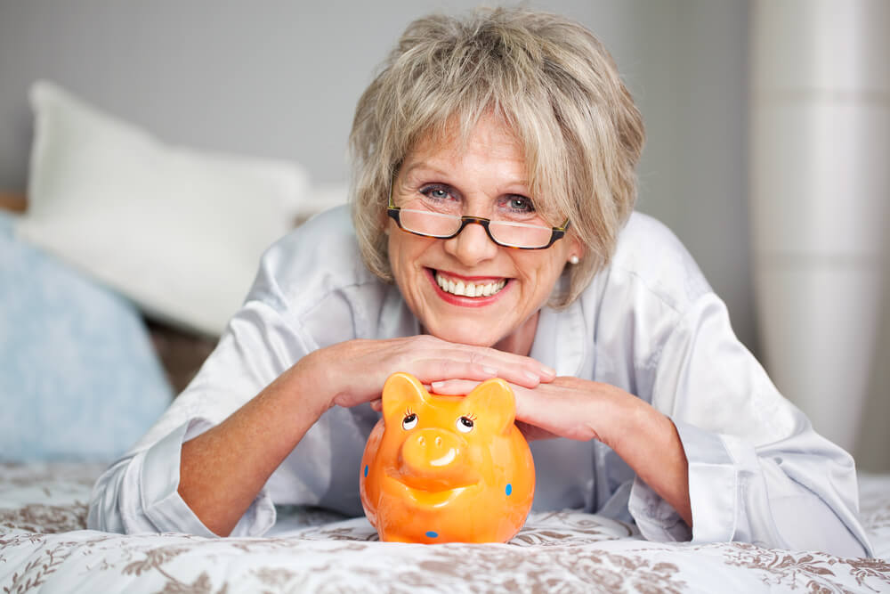 eldre person som lener seg mot en oransje gris med blå prikker og smiler. skal spare til pensjon