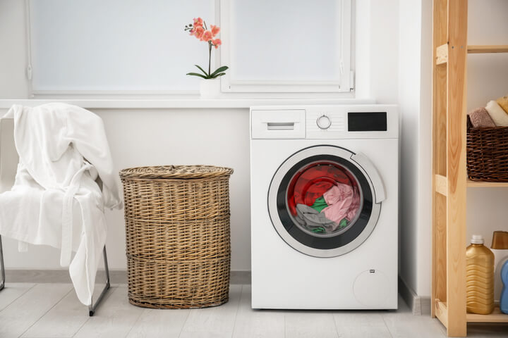 En fin vaskemaskin ved siden av en stråkurv i oppvaskrommet